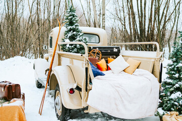 beige retro pickup truck decorated for Christmas and New Year with vintage interior items, suitcases, skis, sledge, blankets, Christmas ornaments, winter time © klavdiyav