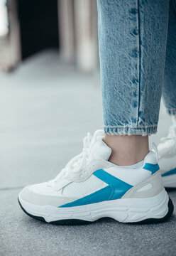A woman wearing stylish white sneakers on the street .Women's sports shoes. Fashionable sneakers on female legs. Close-up photo.
