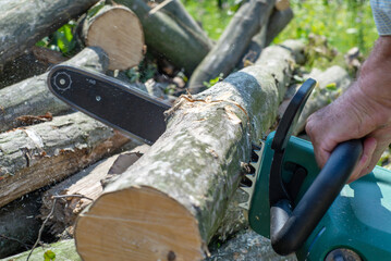 A man is sawing a tree with a chainsaw. A young near his house