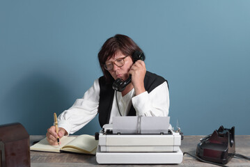 A secretary from the past at work. Table with telephone and typewriter. Vintage