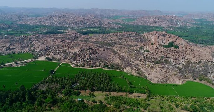 Aerial shot of Hampi temple complex with rocky hills, rice fields, river