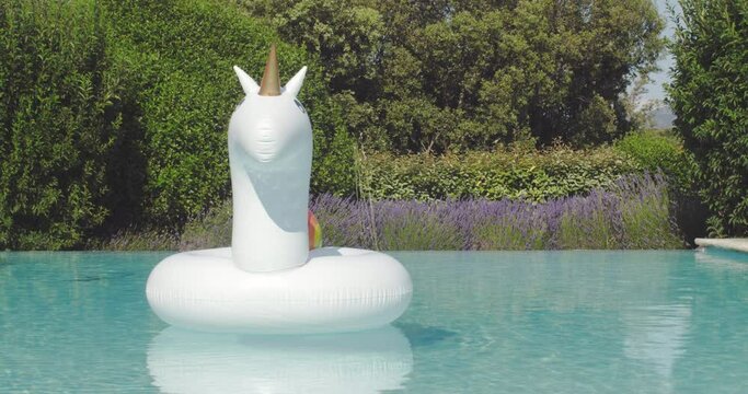 Inflatable colorful white unicorn at the swimming pool. Vacation time in the swim pool with plastic toys. Relaxation and fun concept. Ripple Water in swimming pool with sun. High quality 4k footage