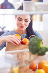 Smiling woman taking a fresh fruit out of the fridge, healthy food concept