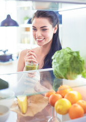 Young woman with glass of tasty healthy smoothie at table in kitchen