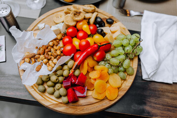 Snack, fresh vegetables, fruits, nuts lie on top of a round wooden board on the table. Food photography.