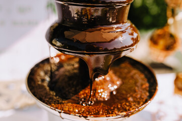 Hot brown milk melted chocolate is poured over the tiers of a fountain close-up for outdoor fondue.. Food photography, dessert.