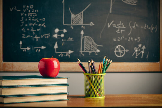 Back to school background with books, pencils and apple over chalkboard and wooden table