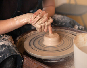 A woman works on a potter's wheel. Hands form a cup of wet clay on a potter's wheel. Artistic concept.