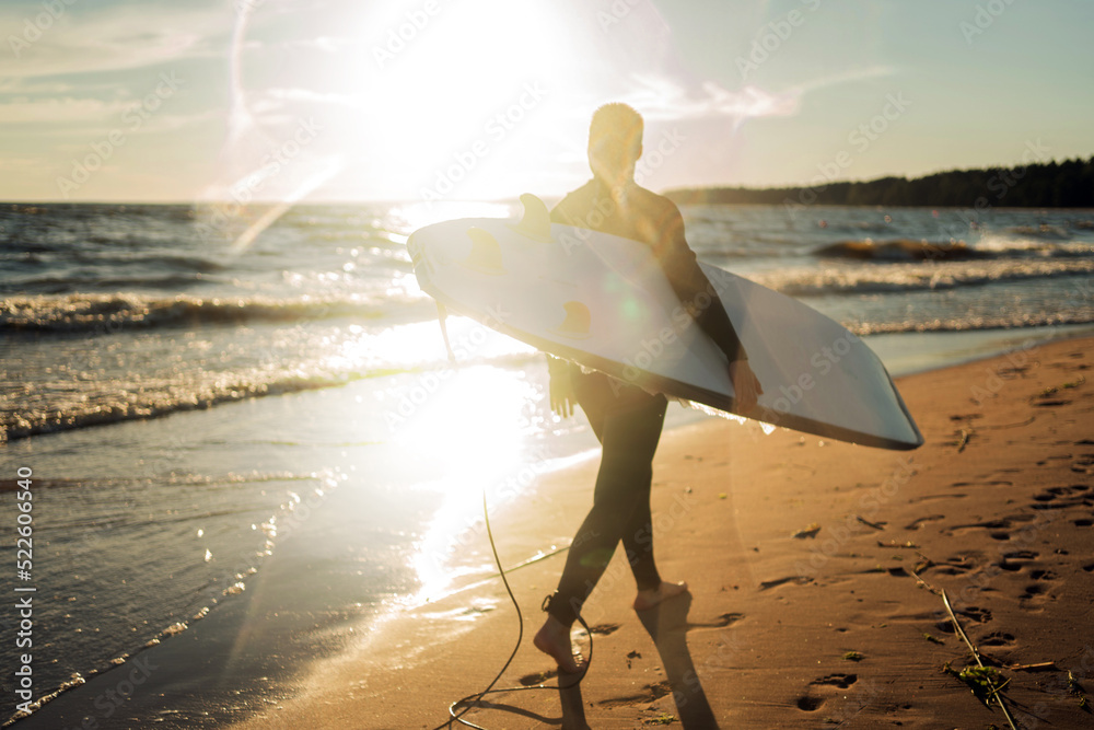 Wall mural A male surfer on a surfboard wetsuit goes to play sports in the sea