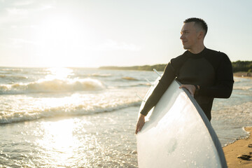 A male surfer on a surfboard wetsuit goes to play sports in the sea