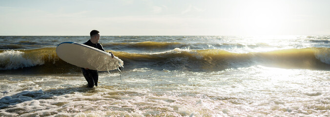 A male surfer on a surfboard wetsuit goes to play sports in the sea