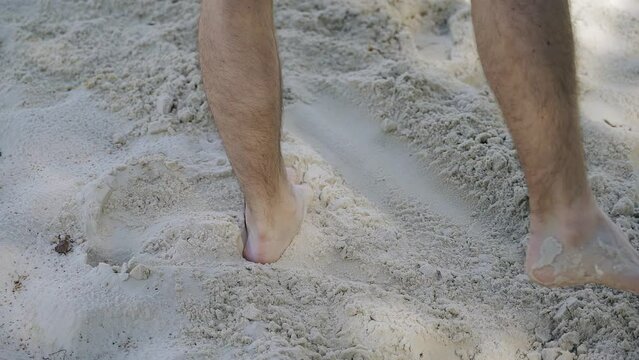 A guy is shoveling sand to the sides on a volleyball court. Taking a close-up of the legs