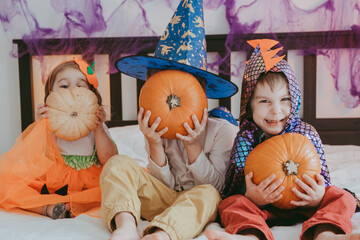 Three little kids in festive halloween costumes with pumpkins having fun. family spending time...