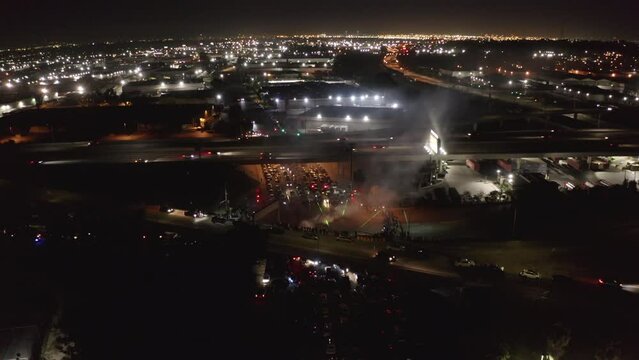 Aerial Shot Of Drag Racing Competition In Illuminated City, Drone Flying Backwards Over Trees At Night -  Los Angeles, California
