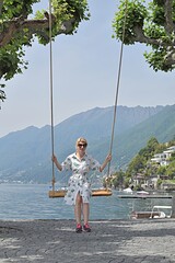 young woman in sunglasses swings on a swing near the lake