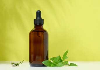 A brown glass bottle with a pipette on a green background. Containers for cosmetics