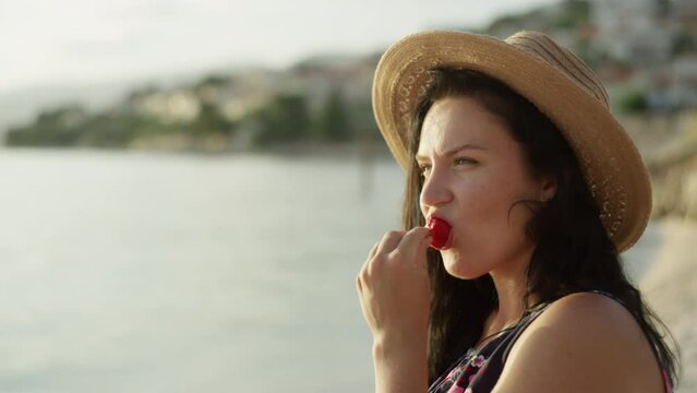 Close-up of a woman on vacation by the sea eating strawberries. Slow motion video of a girl biting a berry in a beautiful ocean landscape. High quality 4k footage