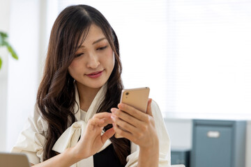 A Japanese woman checking smartphone by remote work in the small office