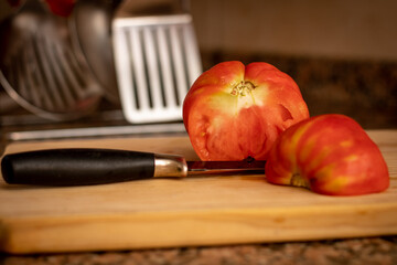 Sliced tomato and a black knife on top of a wood board in a kitchen