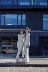 Two happy woman in trendy outfits laugh and walk outside on background of modern building