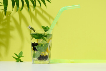 Transparent glass with lemonade, mint leaves, lemon slices and blackberries in the middle.