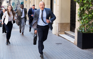Hurrying business people with stressed man in foreground running on city street..