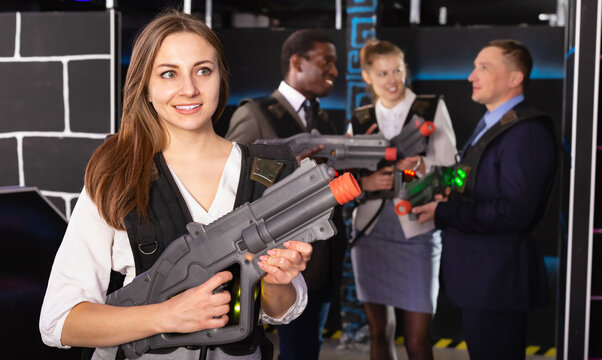 Woman in the business suit holding a laser gun and playing laser tag with colleagues