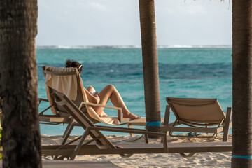 Woman reading a book in tropical beach with sun bed, sun umbrella, turquoise water, at sunset, at 
maldives 2022
