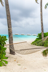Tropical beach summer relax landscape with beach swing or hammock hang on palm tree over white sand sea beach and water bungallows