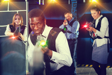 Portrait of African American man playing laser tag with his co-workers in dark room