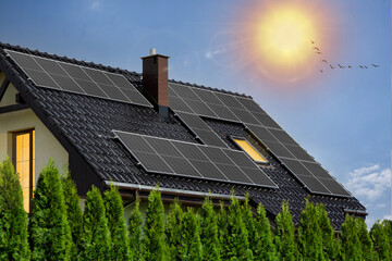 Modern house with black solar panels on roof. Photovoltaic panels on roof. Light in windows, green...