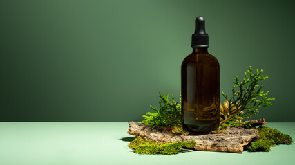 A conceptual composition of essential oil, moss and tree bark on a green background. Oil with serum for skin and hair care. Glass bottle of body oil with a dropper. Self-care and wellness. Copy space