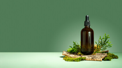 Oil with serum for skin and hair care. A concept of essential oil, moss and tree bark on a green background. Glass brown bottle of body oil with a dropper. Self-care and wellness. Copy space. Banner