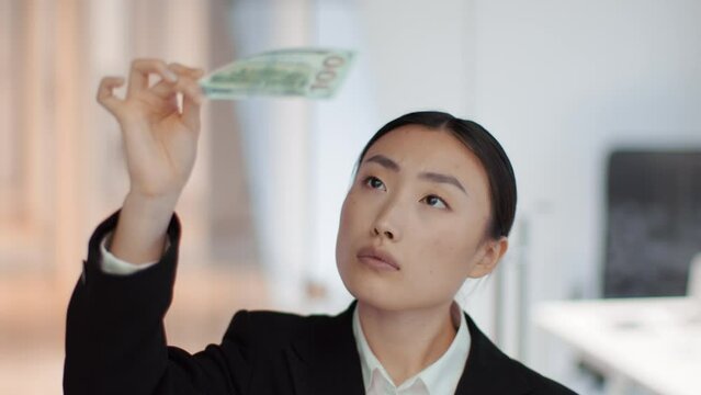 Counterfeit money. Professional asian woman bookkeeper looking at banknote against light, examining currency for fake