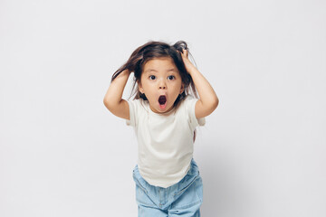 funny, cute, little girl stands in a white T-shirt on a light background and raises her hair on her...