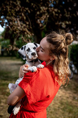 junge Frau in roten Kleid mit jungen Dalmatiner auf dem Arm (Junghund / Welpe)