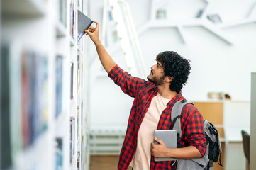 Choosing a book. Clever arabian or indian male student, in casual stylish wear, with a backpack,...