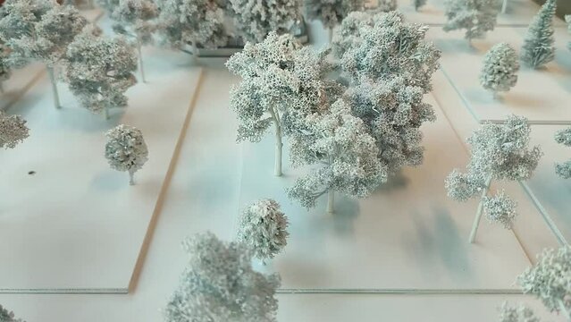 Miniature Mockup Model With Snow Covered Winter Trees On White Foamboard Platforms On The Ground And A Building In The Background - Little Landscape Toy Representation