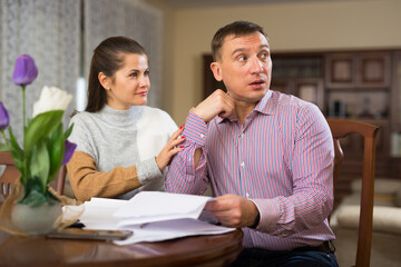 Confused man and woman filling out papers in living room at home