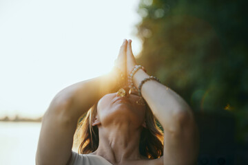 A yogi woman holds her hands in a namaste position and prays while exercising yoga on the dock near...