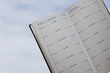 Pages of an agenda in French, English, Spanish, Italian and German with the cloudy sky in the...