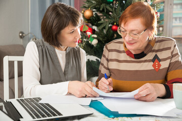 Portrait of friendly happy family of mature woman and her adult daughter sitting at home table, working with papers