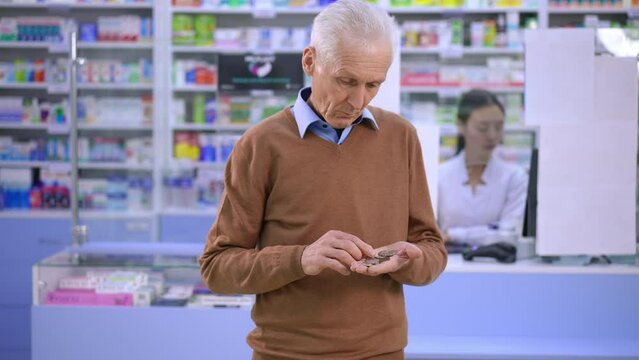 Portrait of frustrated depressed senior man counting coins sighing leaving pharmacy. Sad Caucasian aging client walking away without purchase. Poverty and health care concept