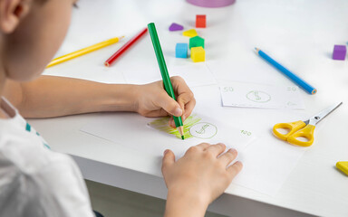 A little boy enthusiastically draws toy money with colored pencils for the game. Family budget. Economy. Money. The kid draws. Economic crisis. Kids play. Selective focus.