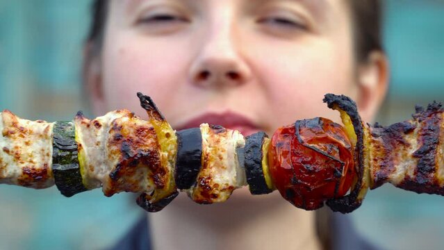Girl eating shish kebab close-up. Young woman tastes meat and vegetable kebab