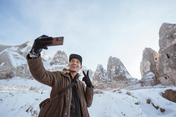 man taking a picture of him self with cave as the background in cappadocia