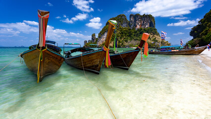 Fototapeta na wymiar Three long tail boats await tourists on the beautiful islands and emerald crystal clear waters of Krabi, Thailand.