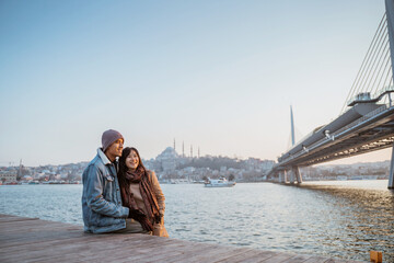 young couple relaxing on the side of bosphorus during sunset. beautiful woman and man with istanbul...