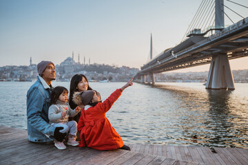 Naklejka premium happy asian family sitting on the side of bosphorus looking at beautiful sunset in istanbul turkey