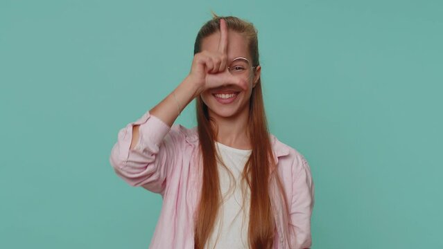 Teenager young girl showing loser gesture and pointing on you, blaming accusing for unsuccess, expressing disrespect, mocking your failure, bullying abuse. Student child kid on blue studio background